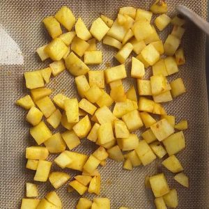 Turmeric coated potato cubes spread in a single layer on a silicone lined baking sheet