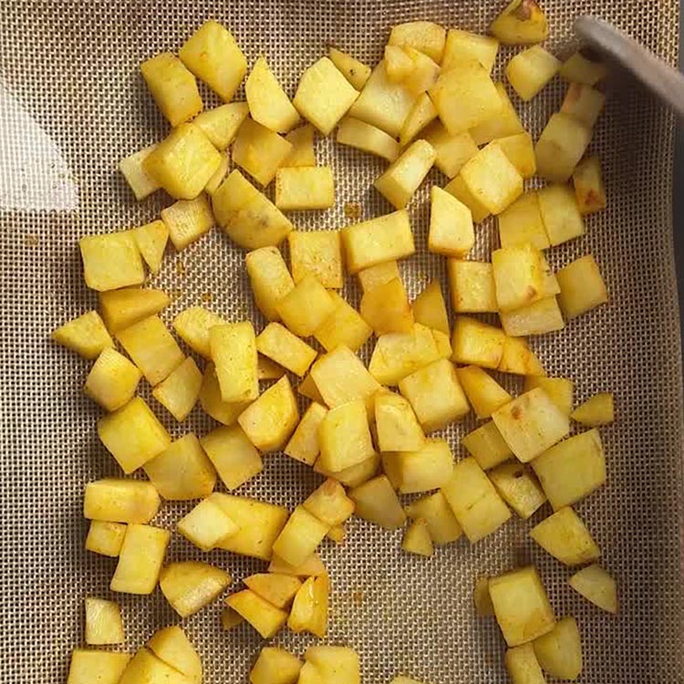 Turmeric coated potato cubes spread in a single layer on a silicone lined baking sheet