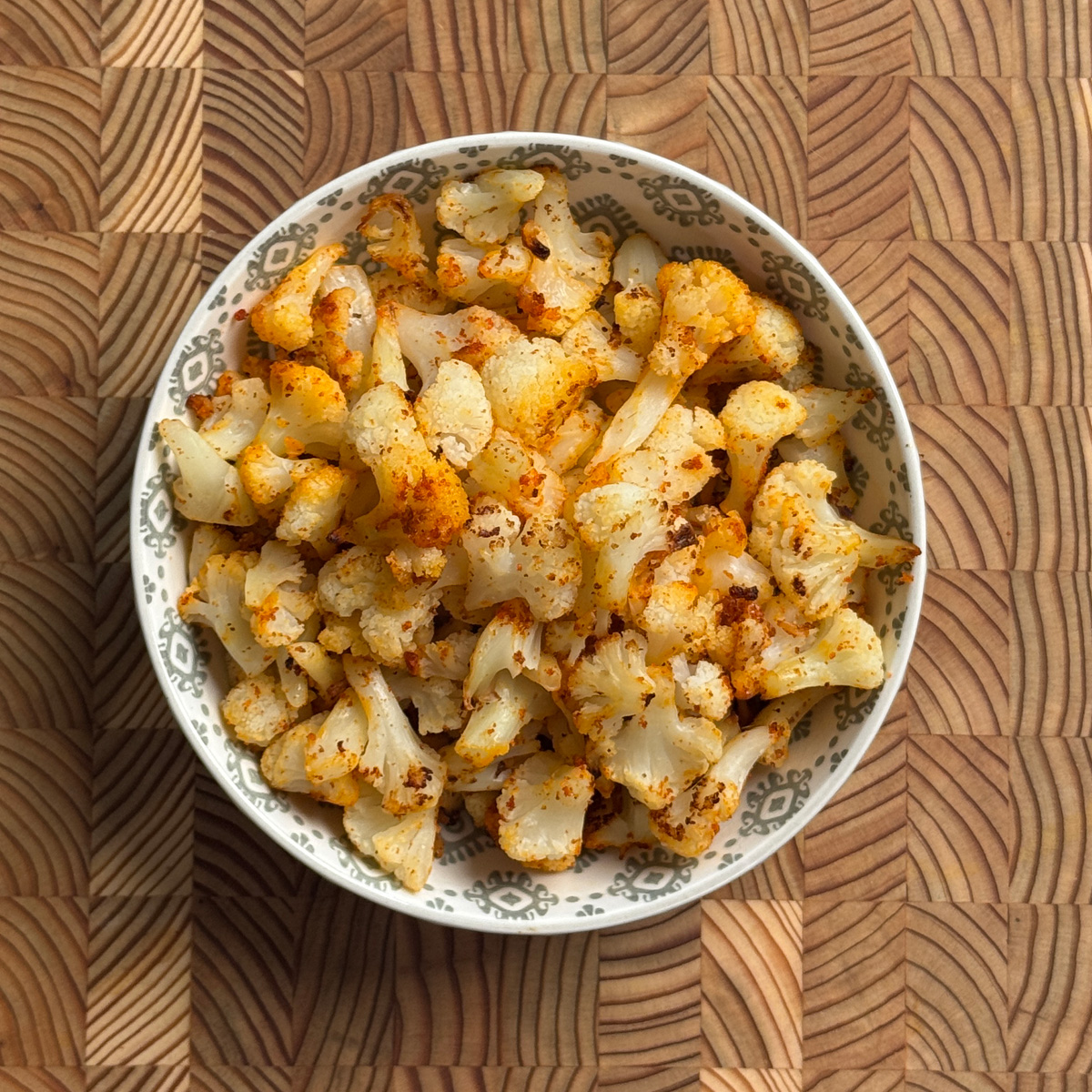 Baked frozen cauliflower with garlic chili powder served in a patterned bowl, overhead view
