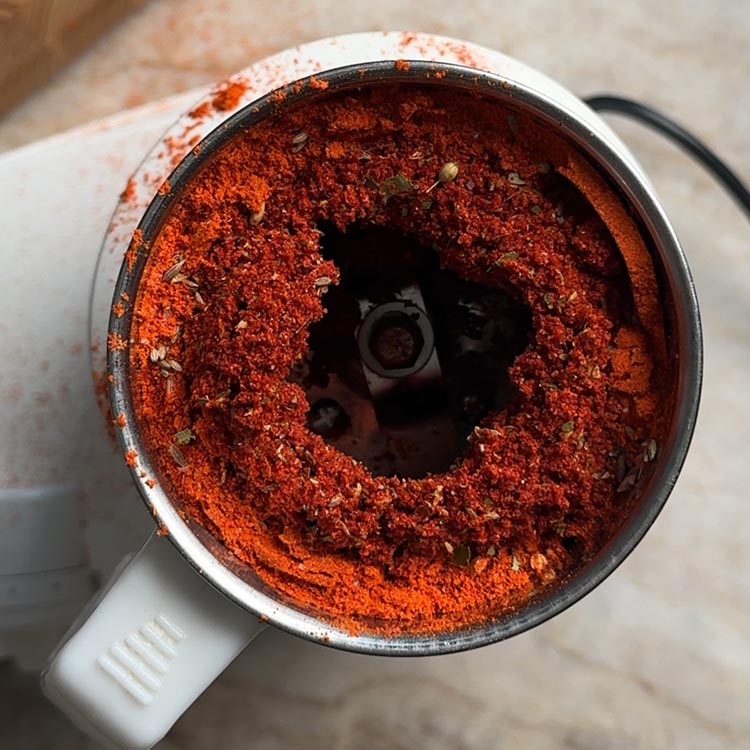 Bright red spice powder inside an open mixer grinder jar after grinding, blade visible in center