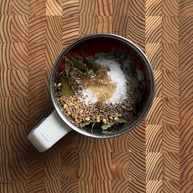 All podi ingredients loaded into a mixer grinder jar: cumin seeds, coriander seeds, curry leaves, chili powder, salt and castor oil visible from above