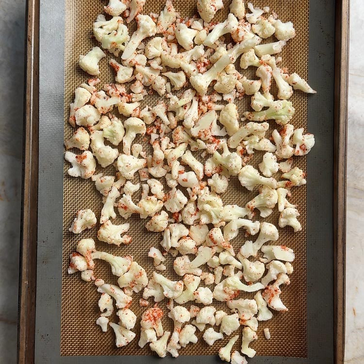Seasoned frozen cauliflower spread in a single layer on a sheet pan before baking