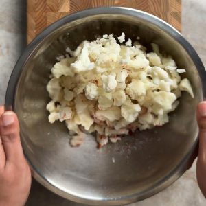 Hands holding a mixing bowl of frozen cauliflower tossed with garlic chili powder and salt