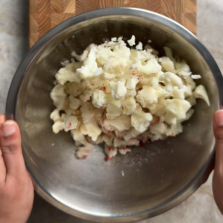 Hands holding a mixing bowl of frozen cauliflower tossed with garlic chili powder and salt