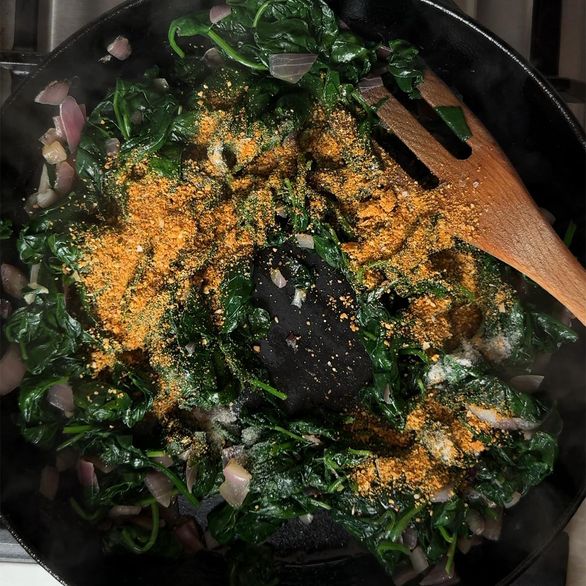 Golden Andhra spice podi spice powder being added on top of wilted spinach in a pan