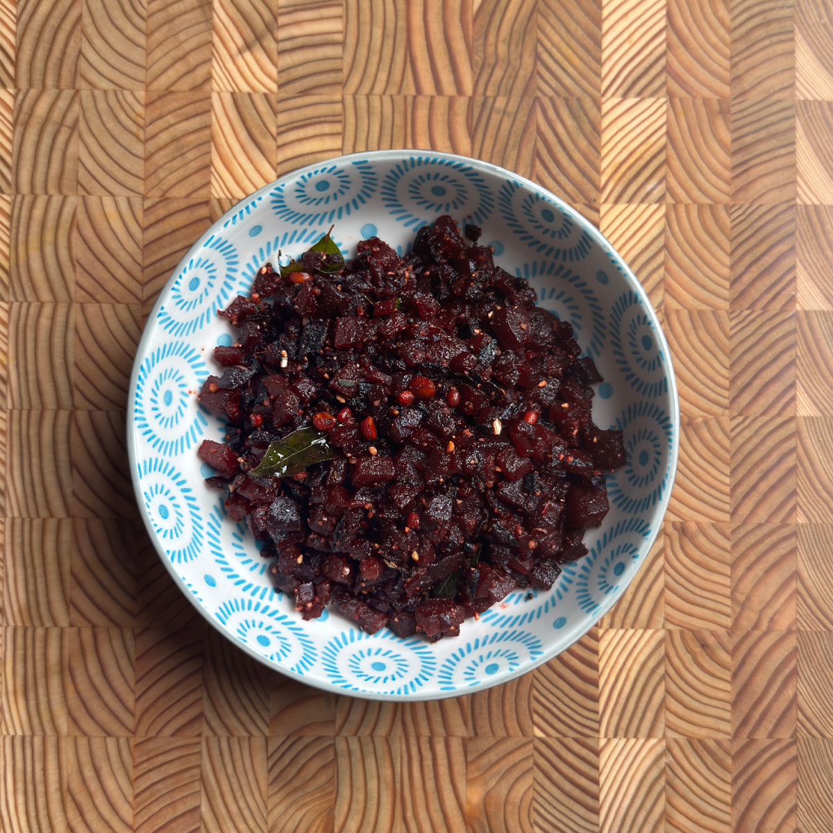 Andhra beetroot fry served in a blue patterned bowl on a wooden cutting board, overhead view