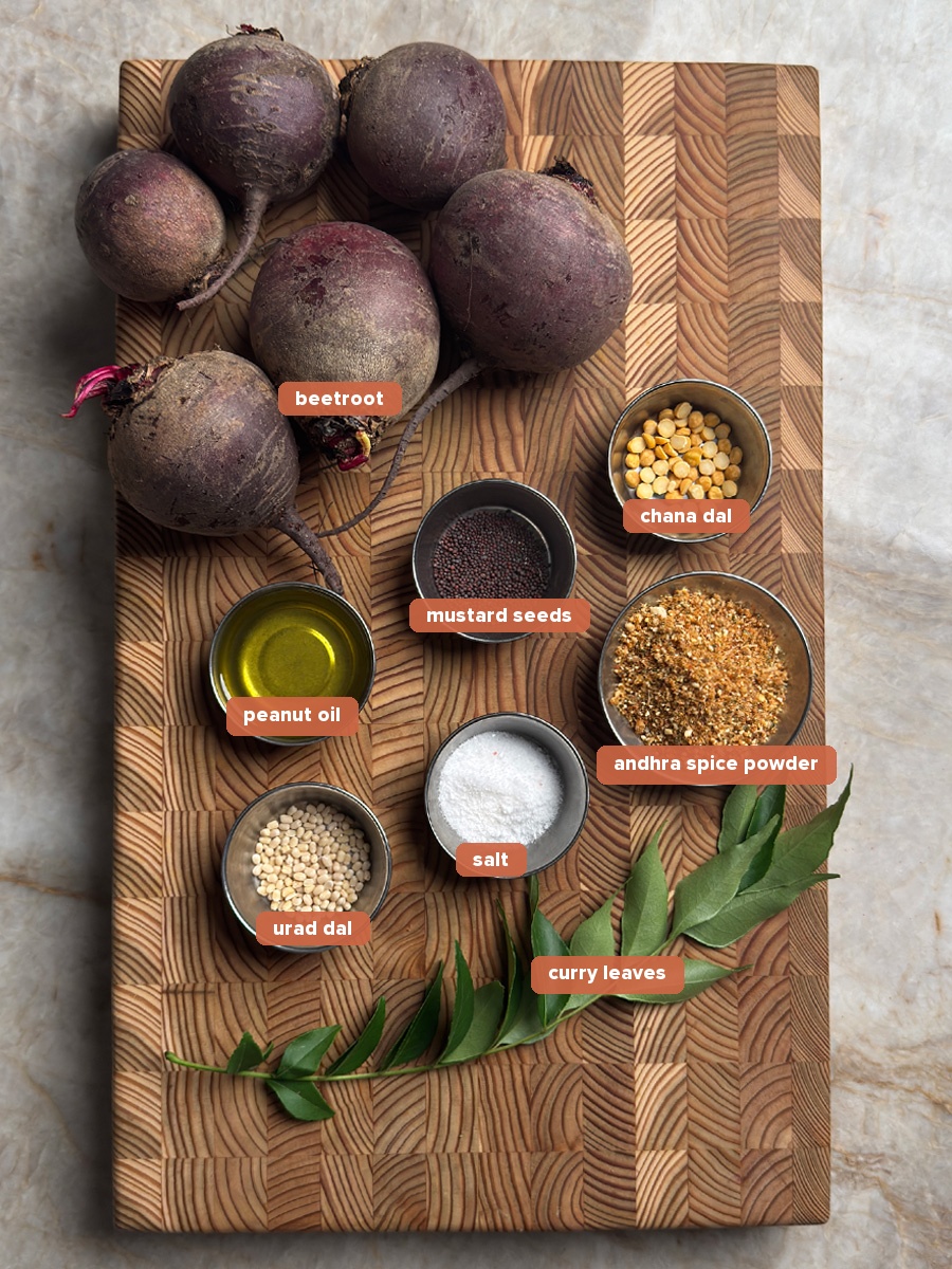All ingredients for andhra beetroot fry on a wooden board, including whole beets, spices, oil and curry leaves