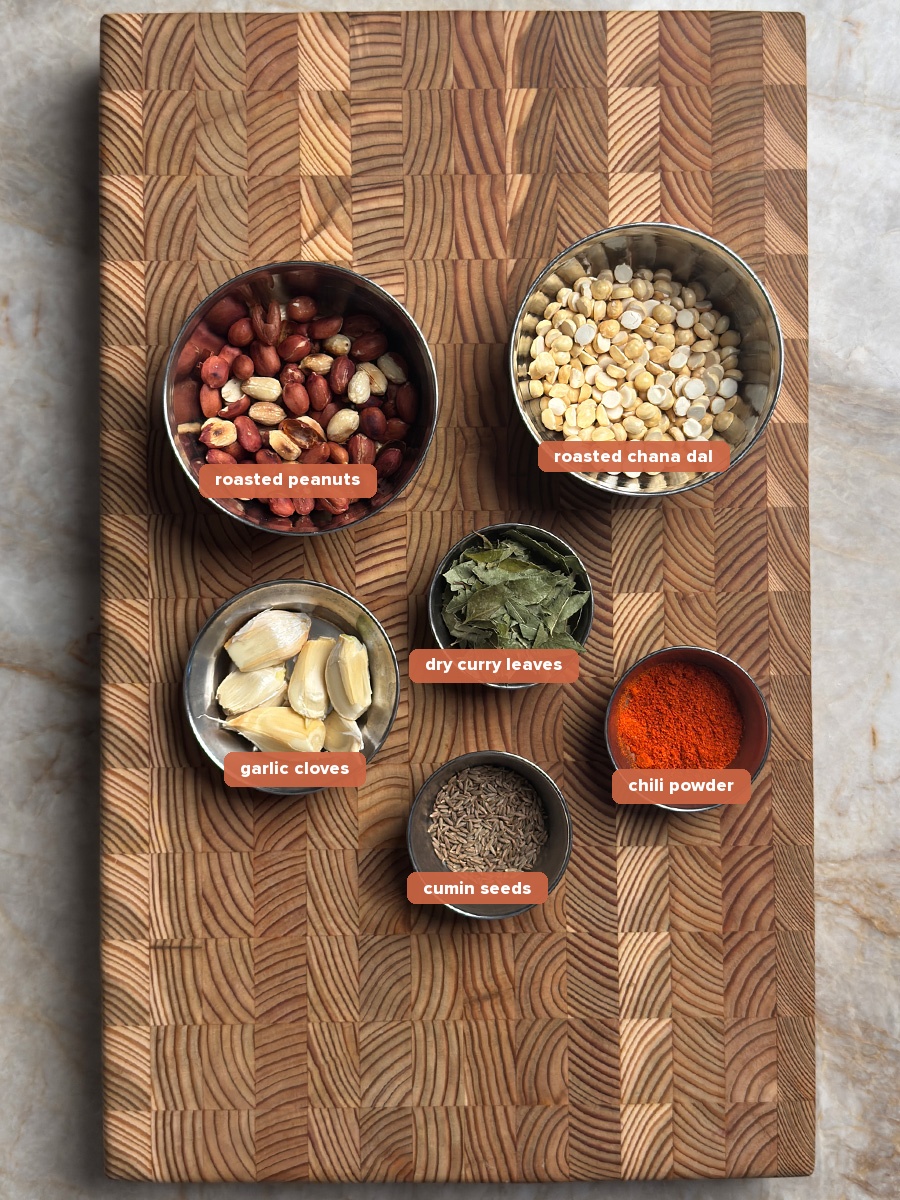 six ingredients for andhra spice powder arranged in small steel bowls on a wooden cutting board