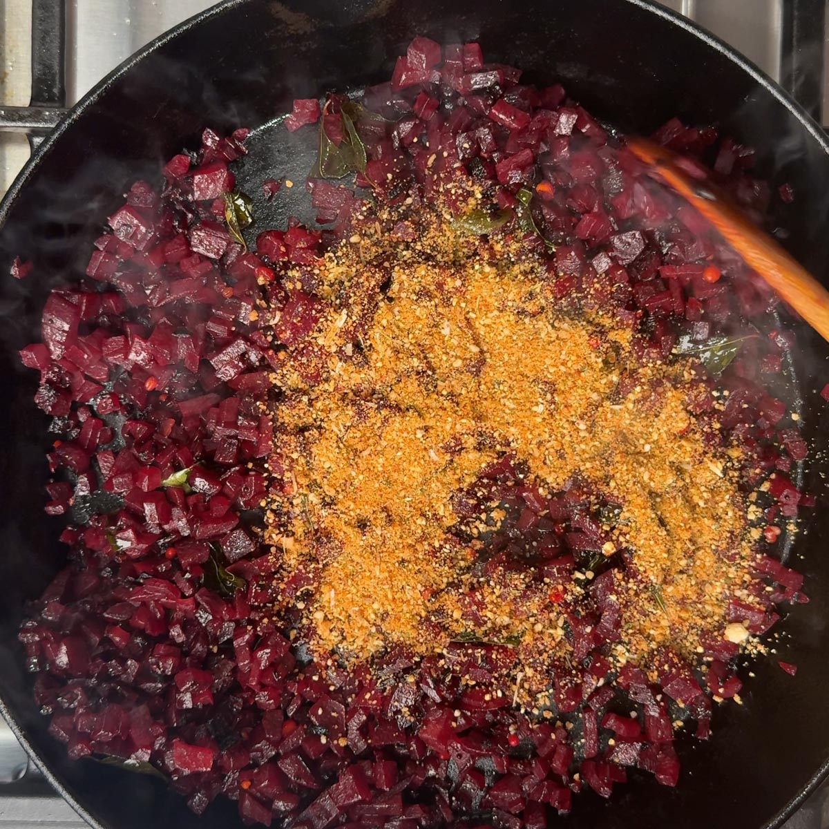 Golden Andhra spice powder piled onto cooked dark red beetroot in a pan before mixing