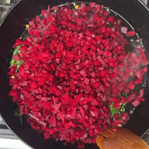 Bright red diced beetroot just added to a pan with green curry leaves visible underneath