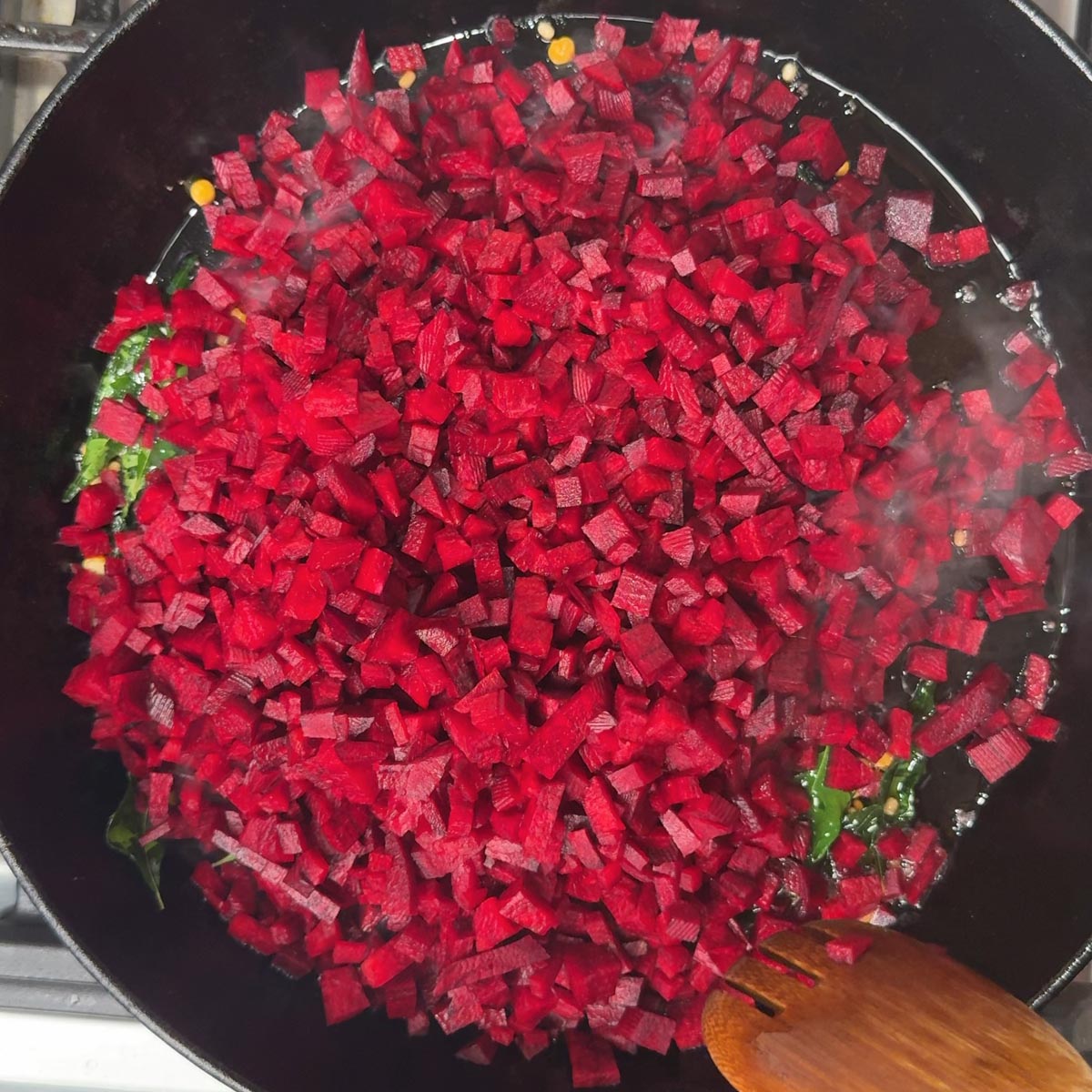 Bright red diced beetroot just added to a pan with green curry leaves visible underneath