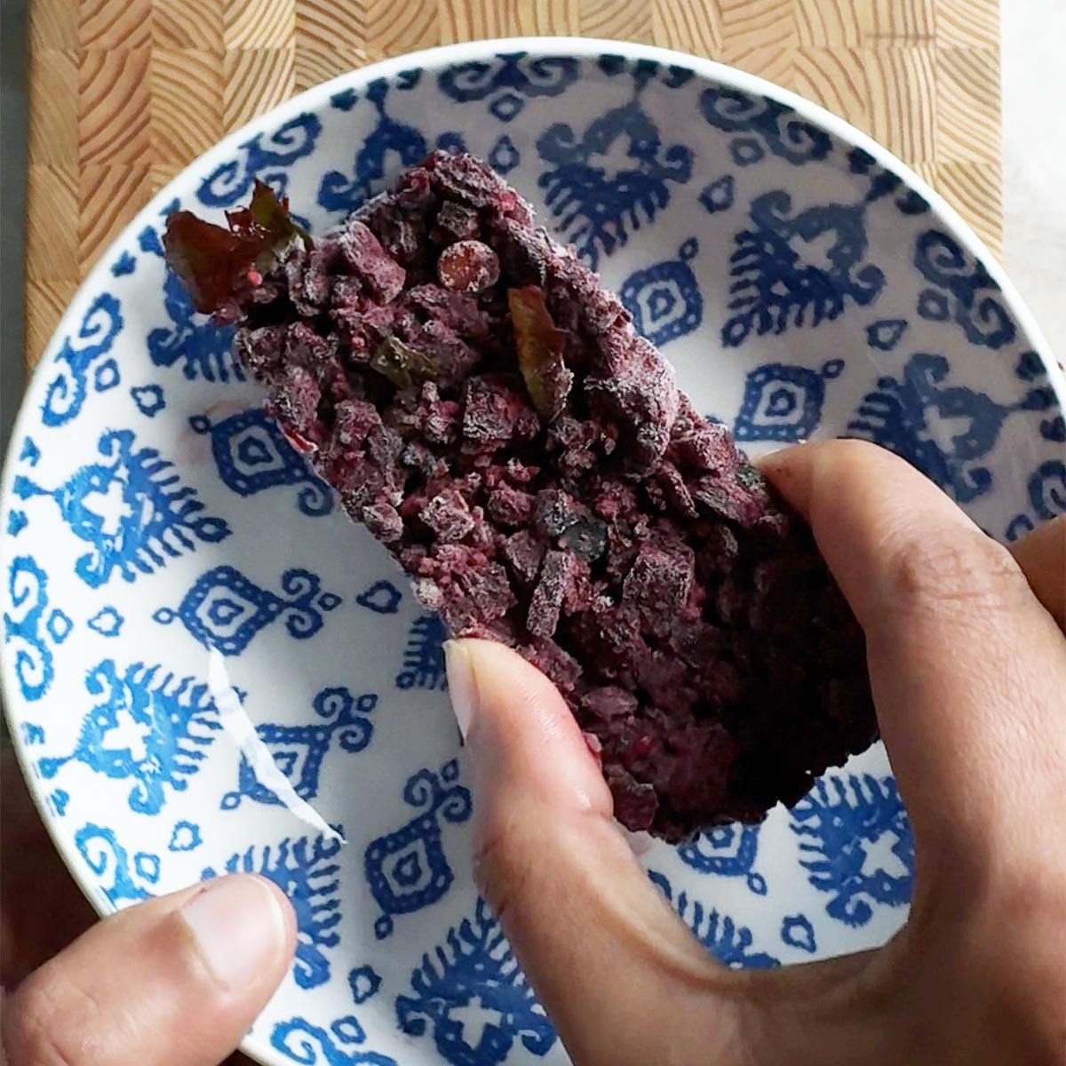 Frozen andhra beetroot fry cube held in hand over a blue patterned bowl, showing the solid frozen portion