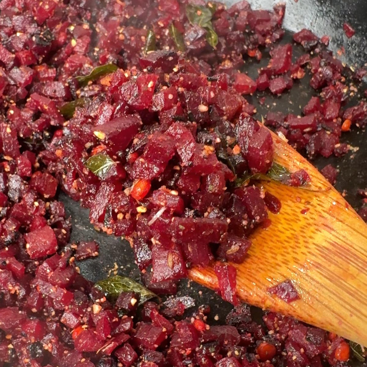 Wooden spoon mixing Andhra spice powder into cooked beetroot in a black pan