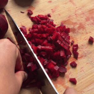 Small diced raw beetroot being cut on a wooden board, showing bright red pieces and a knife