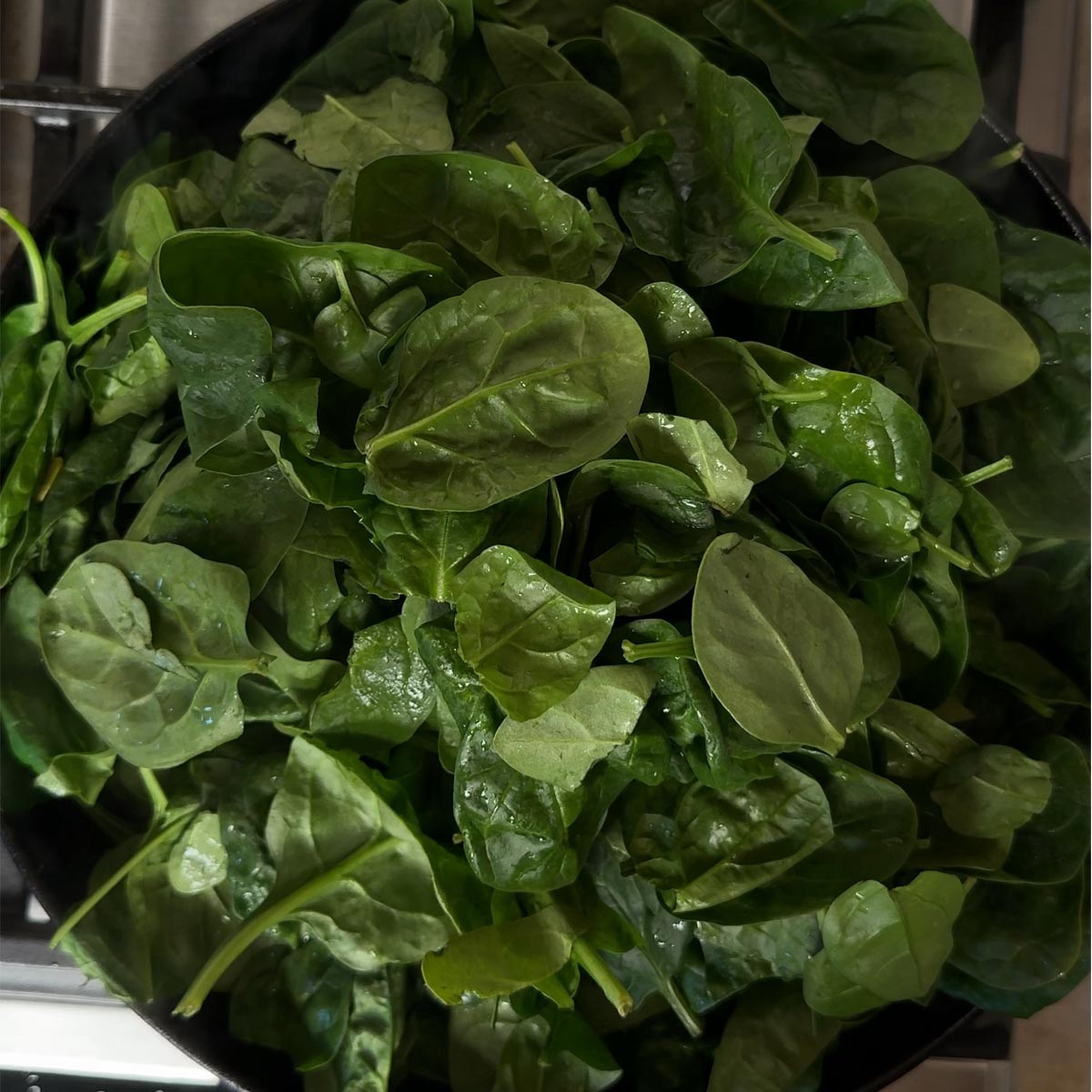 A full pan of fresh baby spinach leaves before cooking, overhead view