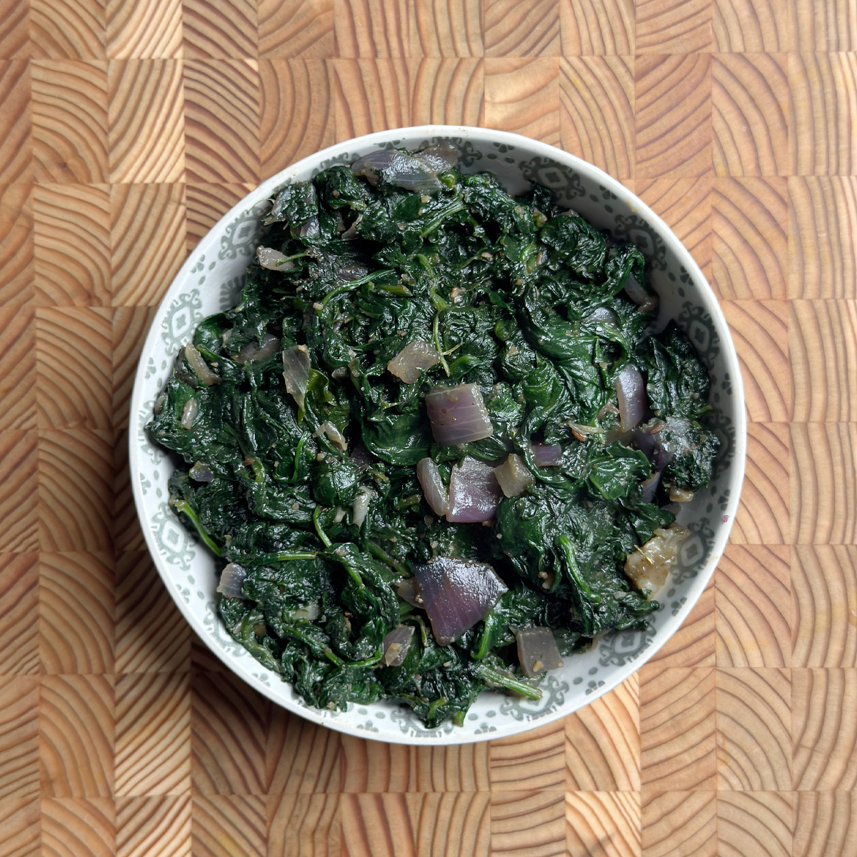 Andhra spinach fry served in a white bowl on a wooden cutting board, overhead view