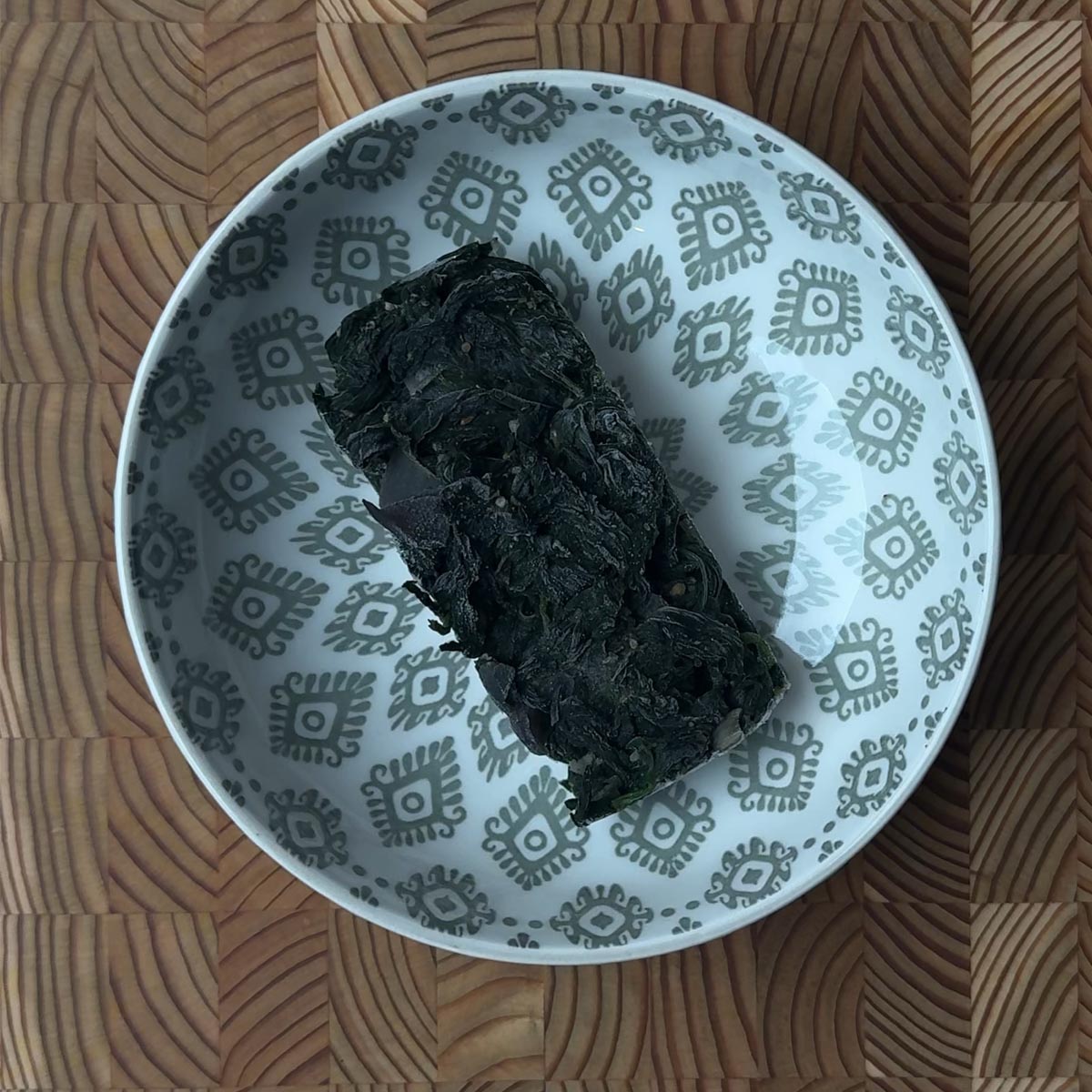 A frozen spinach fry cube sitting in a white decorative bowl before reheating