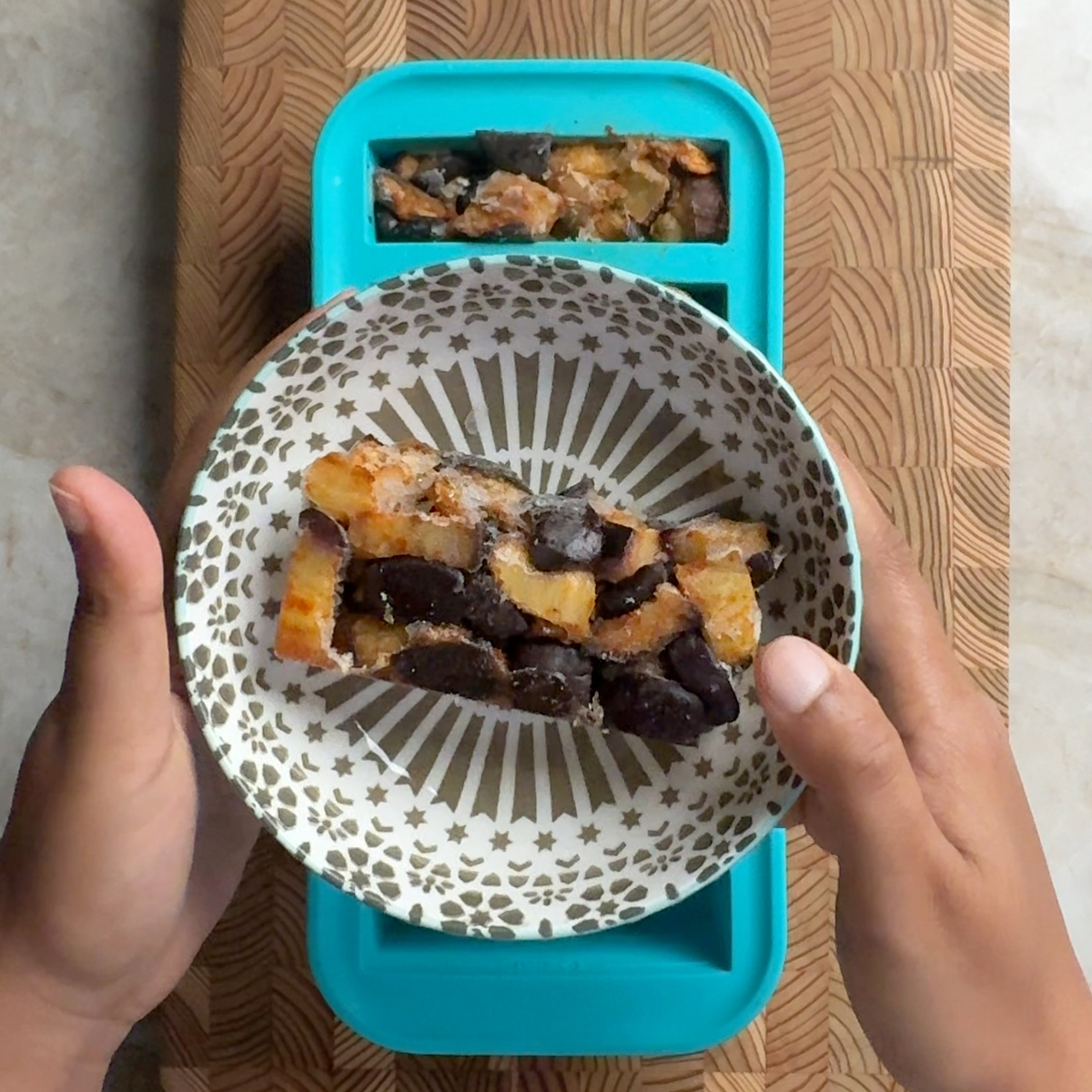 Hands holding a small bowl of eggplant cubes portioned from a Souper Cubes freezer tray