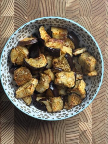 Oven roasted eggplant cubes in a teal patterned bowl on a wooden cutting board, overhead view