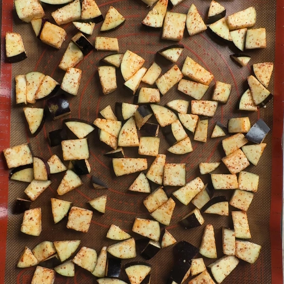 Seasoned eggplant cubes spread in a single layer on a silicone mat before going into the oven