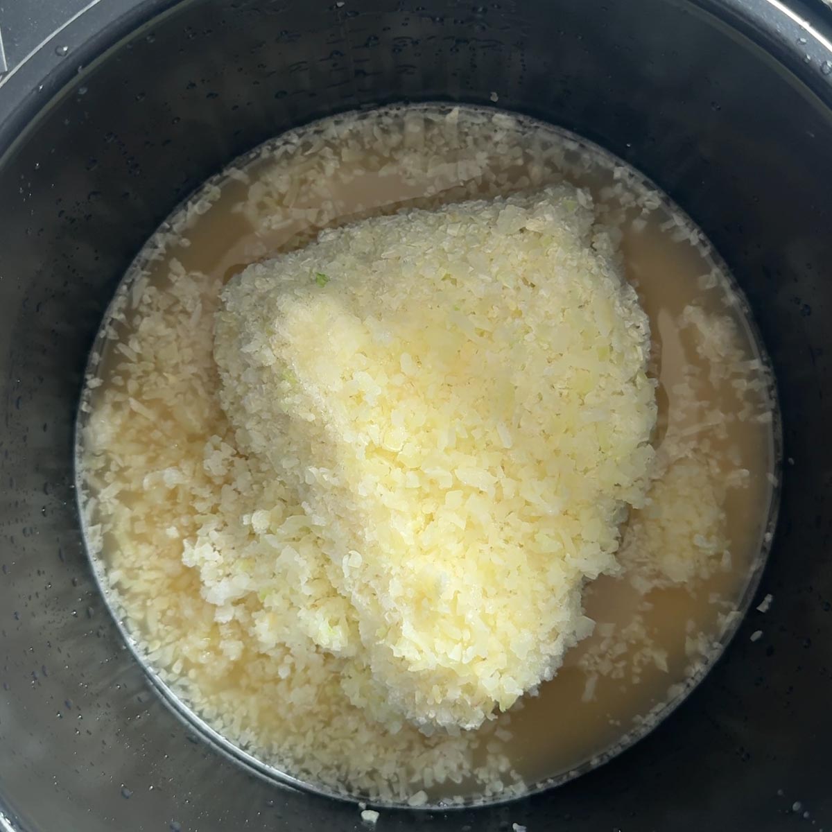 Frozen riced cauliflower added on top of rice and broth in the pot