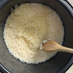 Wooden spoon fluffing cooked rice and cauliflower rice in the pot