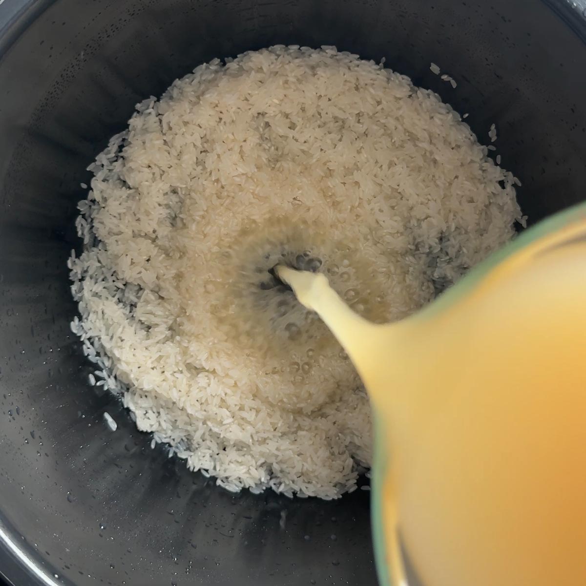 Chicken bone broth being poured over rinsed rice in a pressure cooker pot