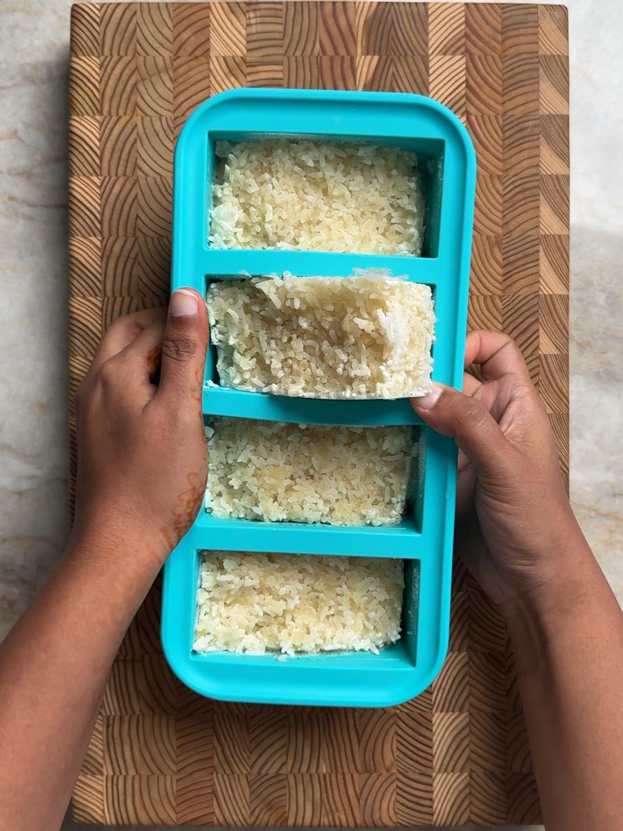 Hands popping a frozen rice and cauliflower rice block out of the tray