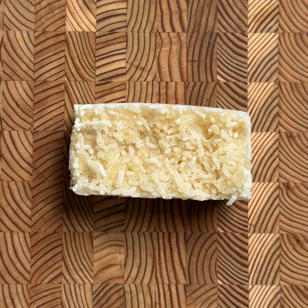 Single frozen rice and cauliflower rice portion block on a wood cutting board