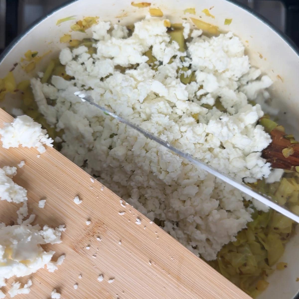 Freshly crumbled paneer being added on top of cooked cabbage in a pot