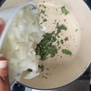 Diced onions being poured into a pot of tempered mustard seeds, cumin seeds, and green chilies.