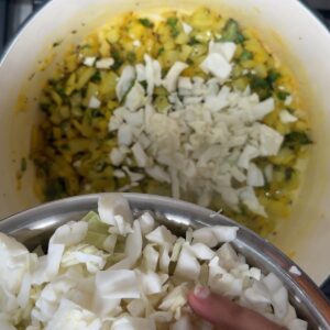 Shredded cabbage being added to a pot of turmeric spiced onions.