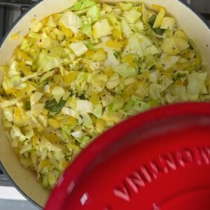 Cabbage cooking down in a pot, partially covered with a red lid.