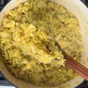 A wooden spoon mixing crumbled paneer into cooked cabbage until evenly combined.