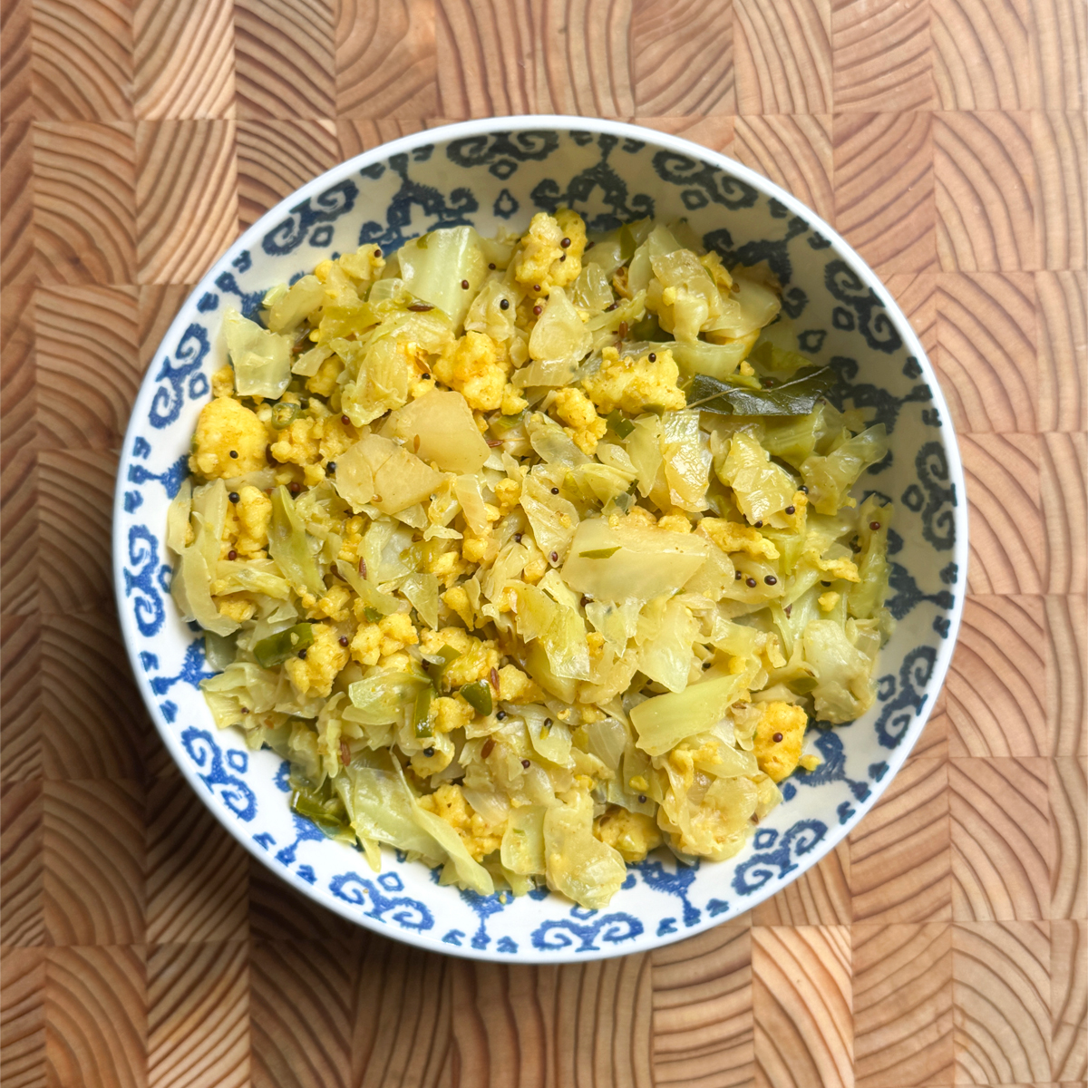 A bowl of cabbage paneer bhurji, a bright yellow scramble flecked with mustard seeds and curry leaves