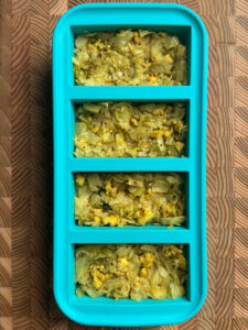 Cooked paneer and cabbage scramble portioned into a teal silicone freezer tray.