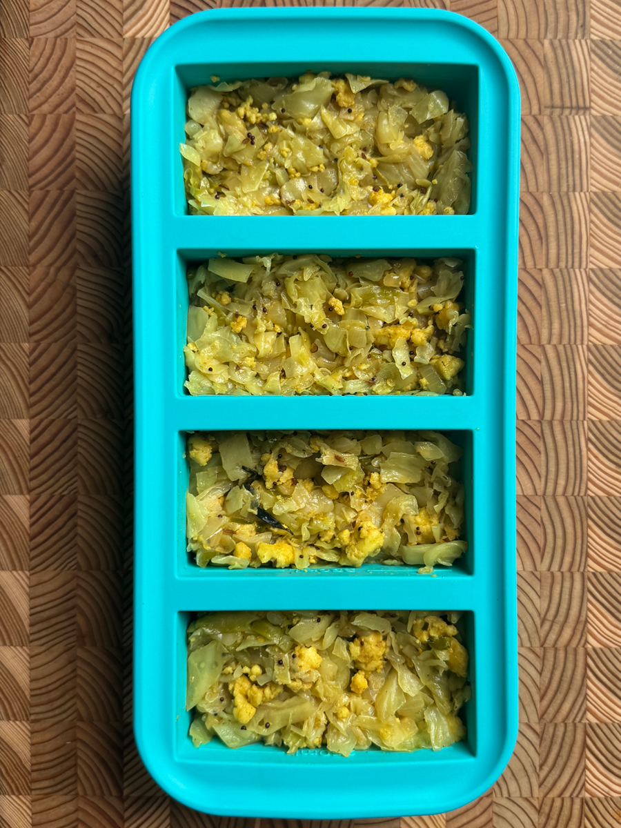 Cooked paneer and cabbage scramble portioned into a teal silicone freezer tray