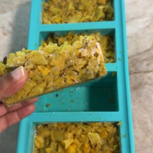 A hand lifting one frozen portion of paneer cabbage scramble out of a freezer tray.