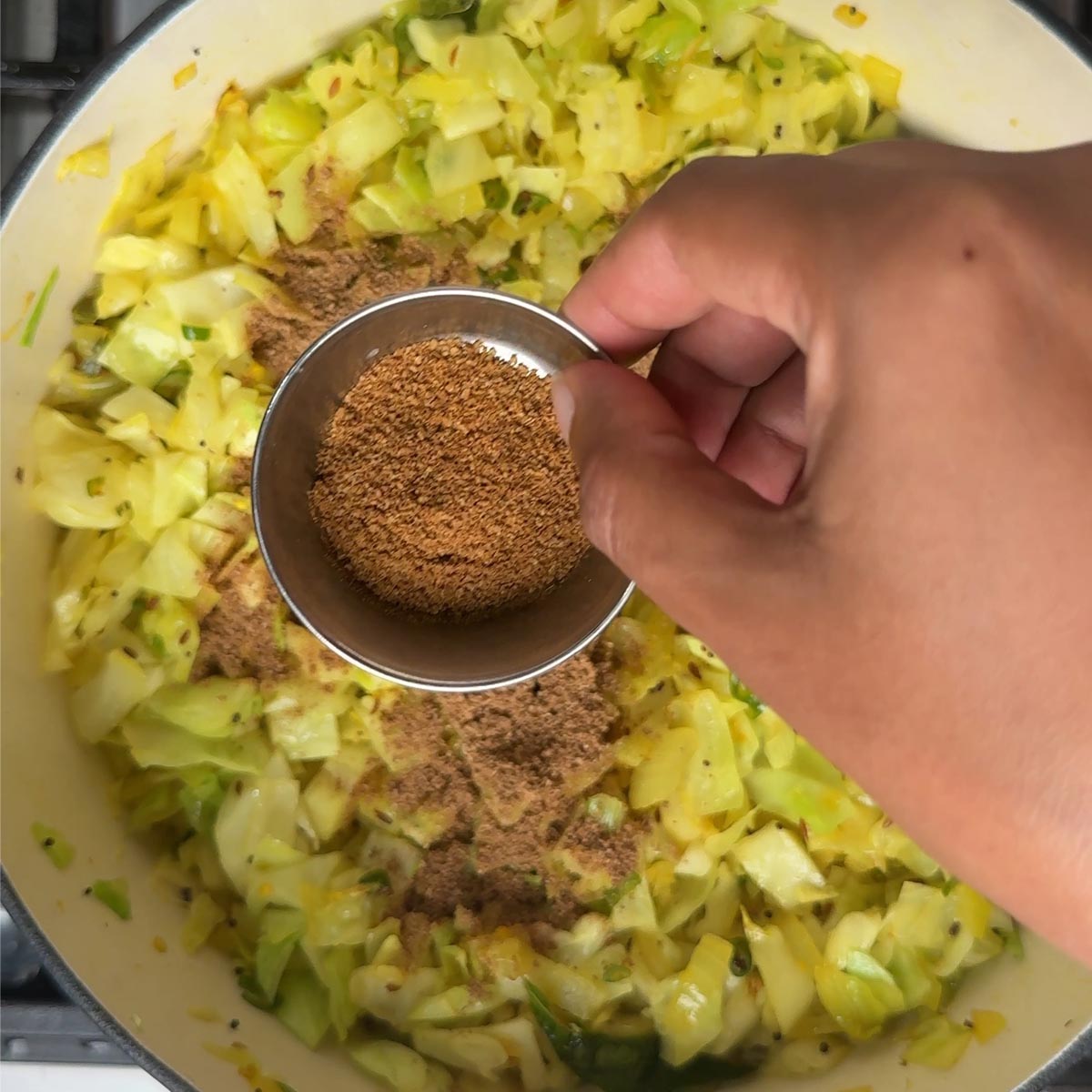 Cumin powder being sprinkled over softened, turmeric colored cabbage