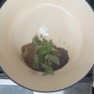 Mustard seeds, cumin seeds, and curry leaves sizzling in oil at the bottom of a pot.