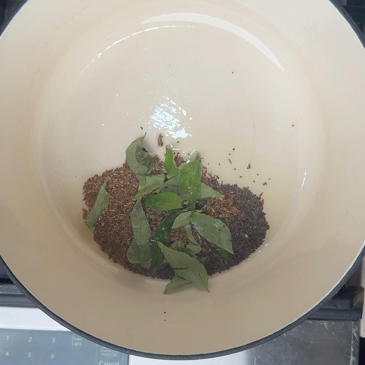 Mustard seeds, cumin seeds, and curry leaves sizzling in oil at the bottom of a pot