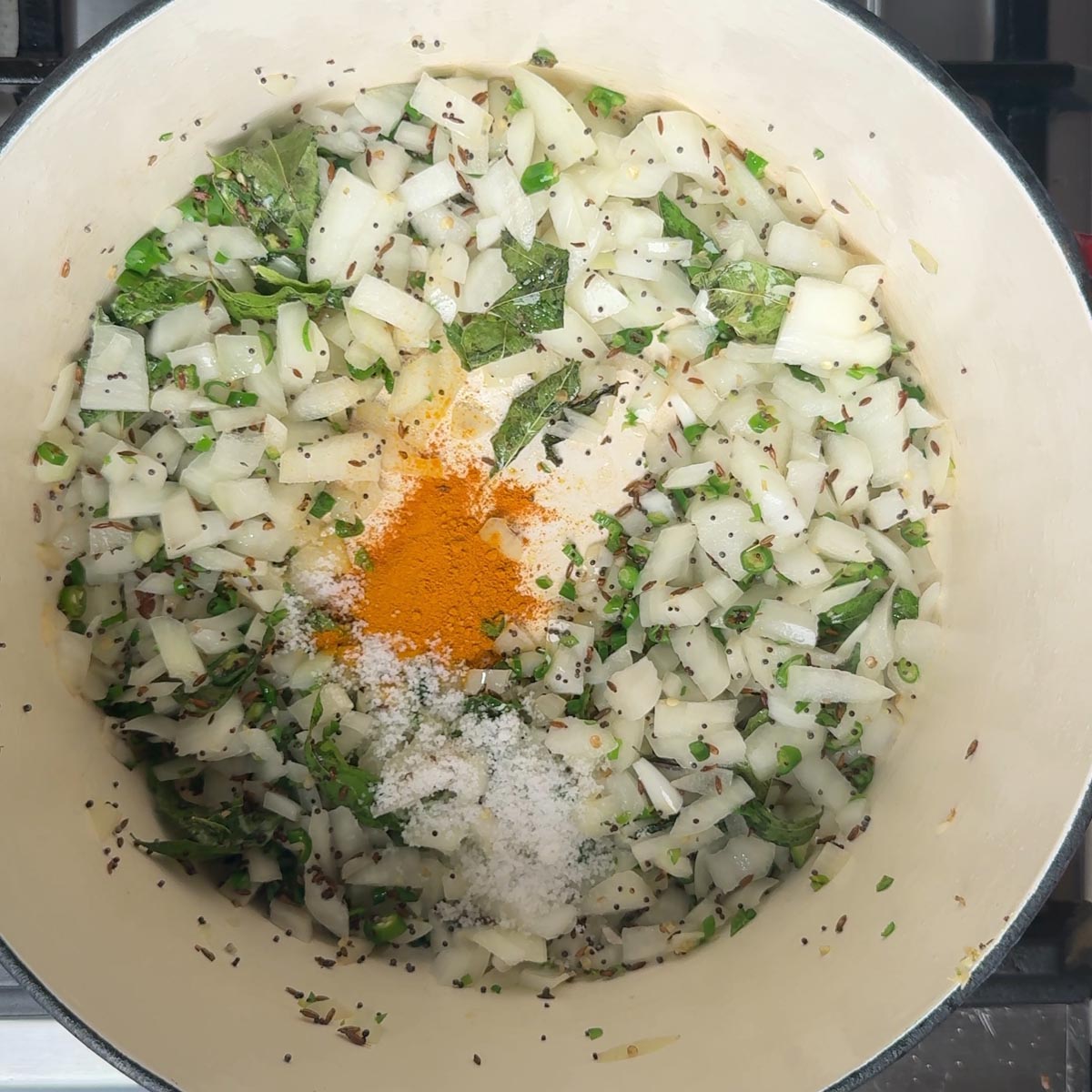 Turmeric powder and salt sprinkled over softened onions in a pot